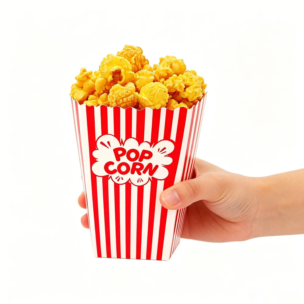A hand holds a red and white striped popcorn box filled with yellow popcorn.
