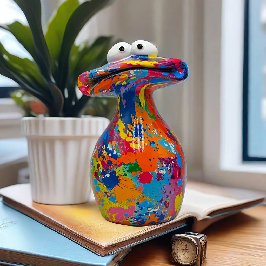 A colorful resin figurine shaped like a frog with a big mouth sitting on a book.