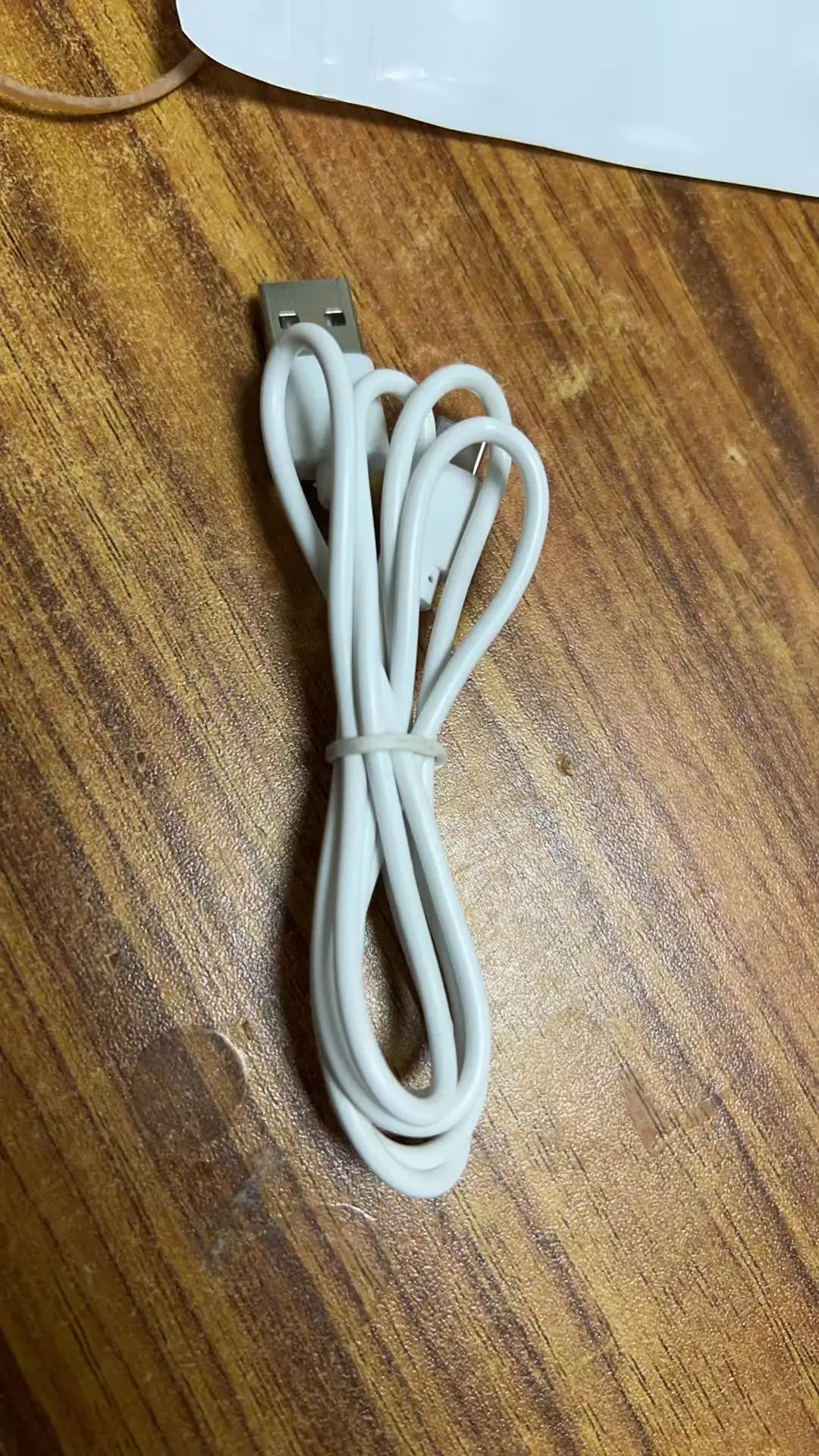 A white rechargeable wearable cooling fan with a clip-on connector and coiled cord lying on a wooden surface.