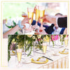 Hands are raising elegant disposable champagne glasses filled with golden liquid at an event.