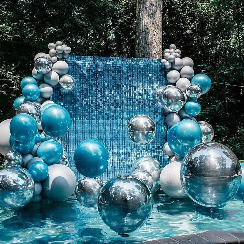 A large arrangement of blue and silver chrome metallic latex balloons floats in clear water against a backdrop of greenery.