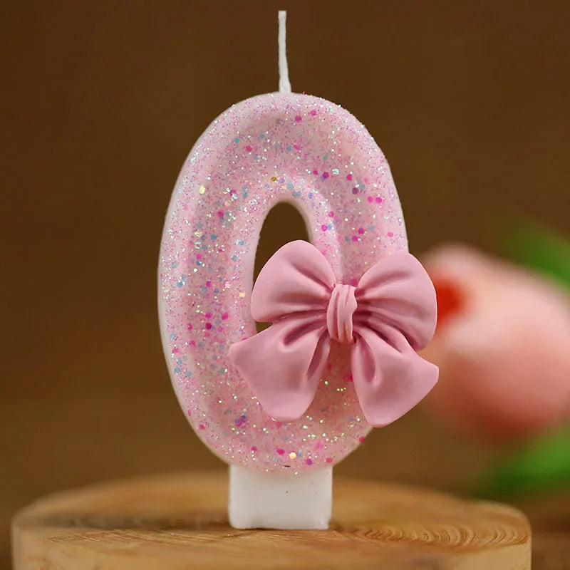 Topper de pastel número 0 brillante rosa con lazo rosa sobre una superficie de madera.