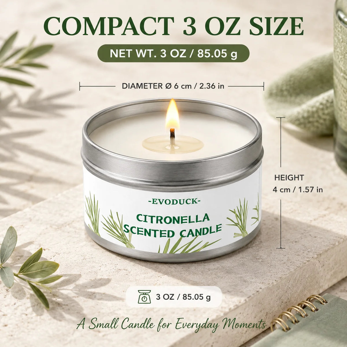 A small silver tin candle with a lit wick and green lemongrass leaves on a light surface.