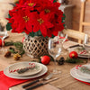 A bouquet of bright red artificial poinsettia flowers in a woven pot set on a rustic wooden table with holiday decorations.