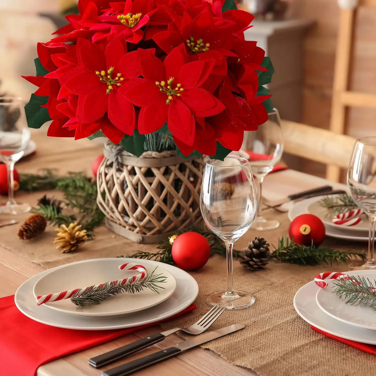 A bouquet of bright red artificial poinsettia flowers in a woven pot set on a rustic wooden table with holiday decorations.