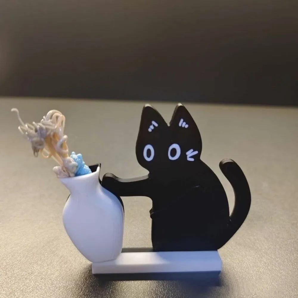 A black acrylic cat figurine with white whiskers is shown next to a white ceramic vase on a gray surface.