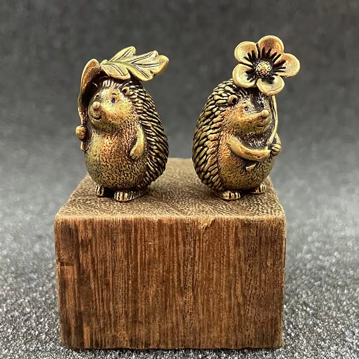A brass figurine set of two hedgehogs with leaf and flower details, resting on a wooden block.