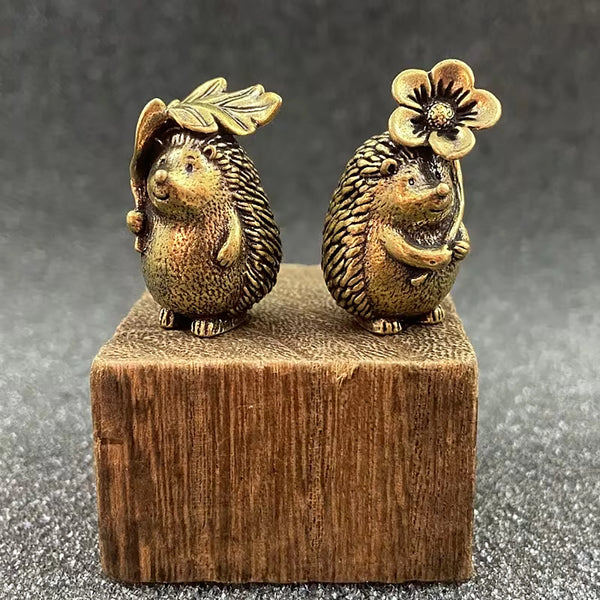 A brass figurine set of two hedgehogs with leaf and flower details, resting on a wooden block.