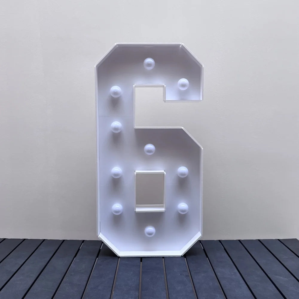 A white light-up marquee number sign shaped like the number 6 mounted on a wall.