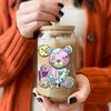 A hand holds a glass jar filled with light beige liquid and a colorful teddy bear decal design.