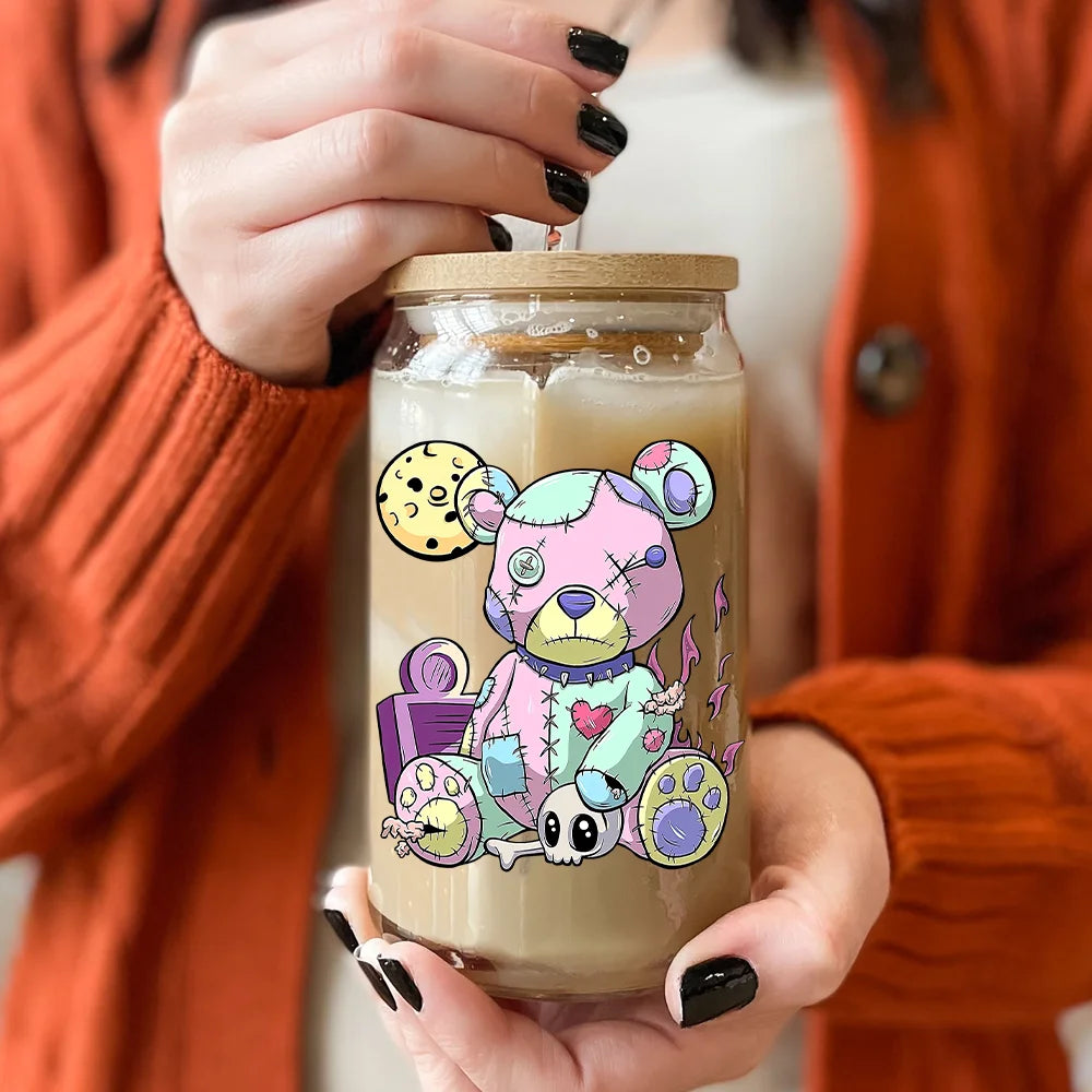 A hand holds a glass jar filled with light beige liquid and a colorful teddy bear decal design.