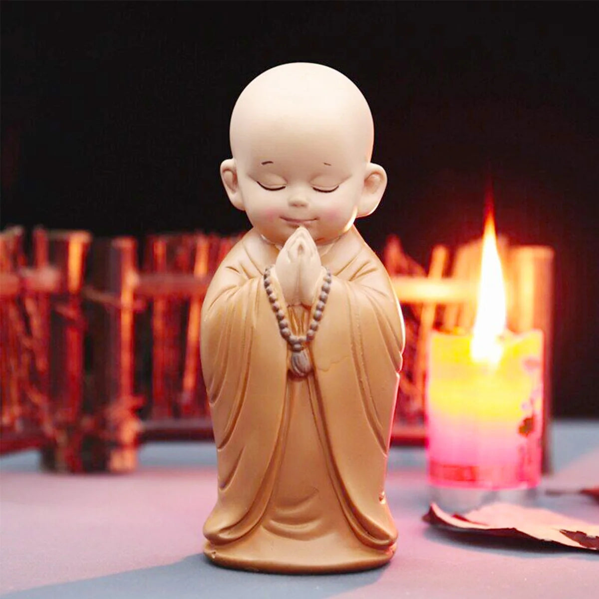 A small, light brown resin figurine of a meditating monk with hands clasped in prayer, set against a dark background with a l