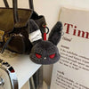 A dark gray bunny plush keychain with black ears and red eyes is displayed next to a leather handbag.