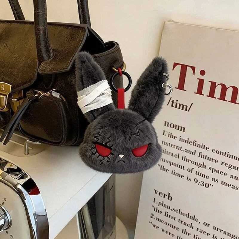 A dark gray bunny plush keychain with black ears and red eyes is displayed next to a leather handbag.