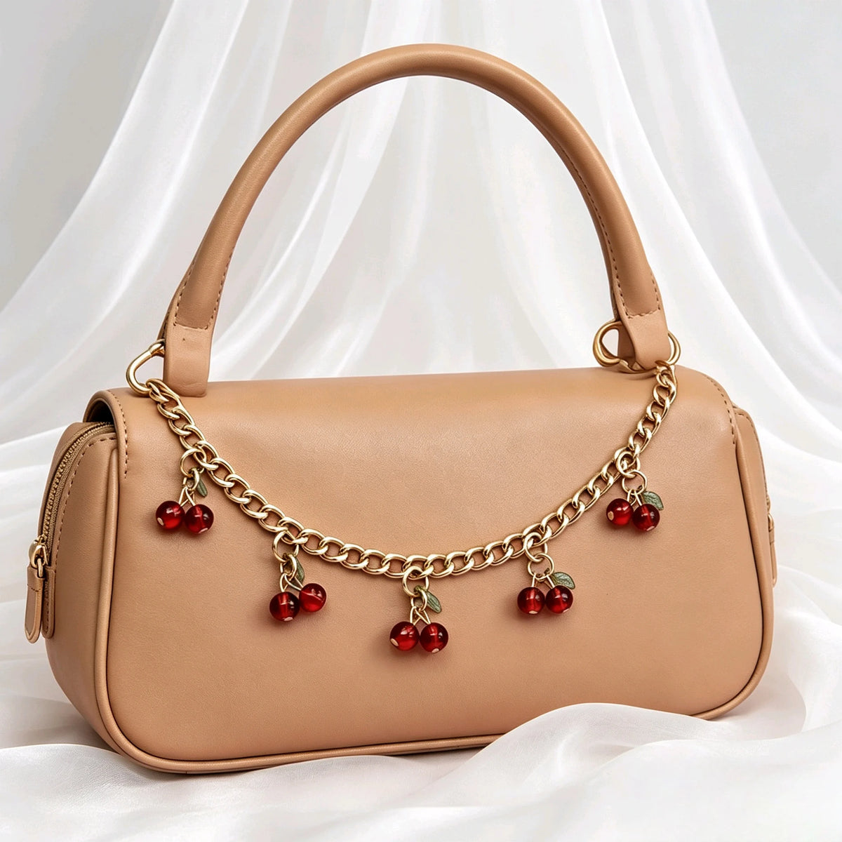 A tan leather handbag with a gold chain and red cherry charms hanging from the strap.