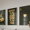 Three framed canvas prints featuring the text LUCKY YOU in gold lettering on dark backgrounds with heart and ace of spades mo
