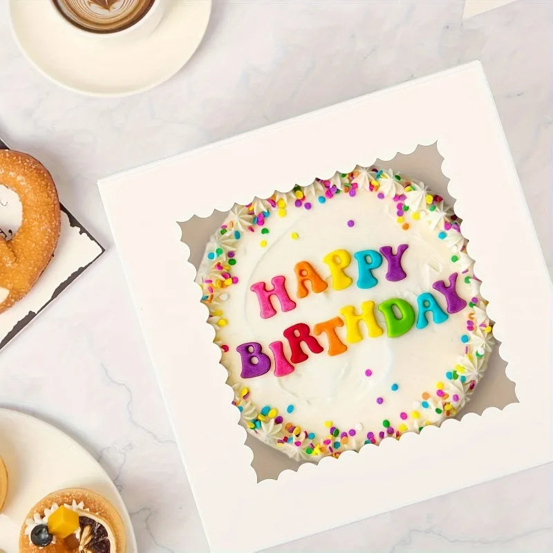 A white birthday cake decorated with colorful sprinkles and the words HAPPY BIRTHDAY, presented in a white bakery box.