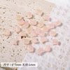 A pile of translucent pink cat head glass beads for jewelry making on white paper.