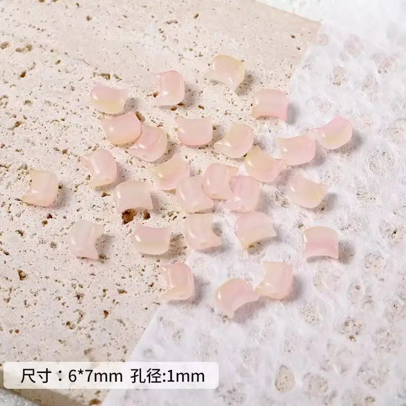 A pile of translucent pink cat head glass beads for jewelry making on white paper.