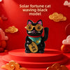 A black cat ornament with gold eyes and a green collar sitting on a red circular base.