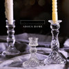 Elegant clear glass pillar candle holders with a white candle and a yellow candle on a gray fabric.