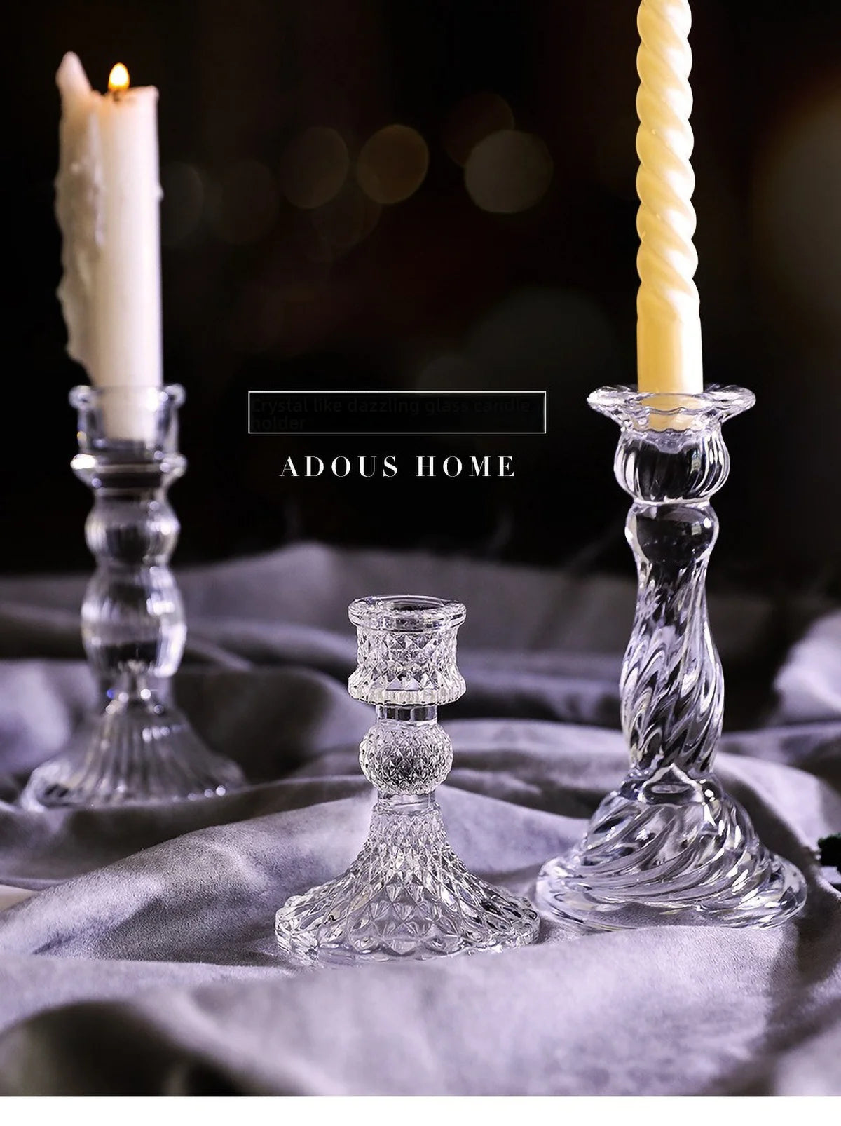 Elegant clear glass pillar candle holders with a white candle and a yellow candle on a gray fabric.