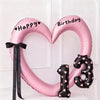 Pink heart-shaped balloon decoration with Happy Birthday text and black ribbon