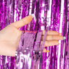 A hand holds several strips of metallic purple tinsel foil fringe curtain backdrop for parties.