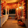 An autumn maple leaf vine garland with warm LED lights hangs over a wooden porch railing and window.