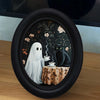 Oval framed wall art featuring a ghost figure and a black cat set against a dark floral background