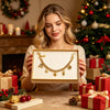 A woman holds a gold multi-charm bag chain accessory box in front of a Christmas tree and wrapped gifts.