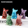A set of three natural crystal dog statues in red, blue, and purple sitting on a white surface.