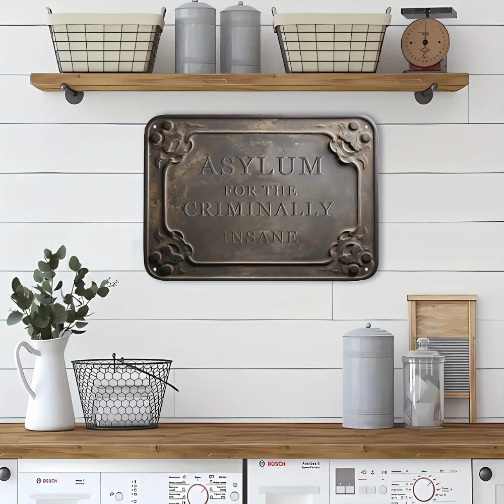 A vintage metal tin sign with the inscription Asylum for the Criminally Insane mounted on a white wooden wall.