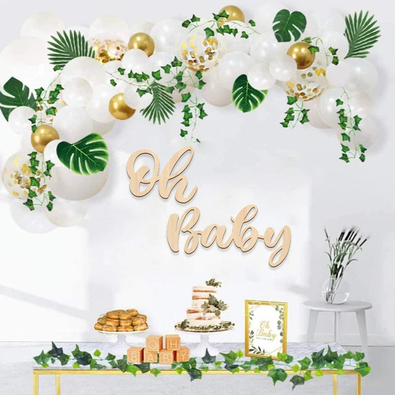 A wooden sign spelling out Oh Baby decorated with white balloons and green foliage for a baby shower
