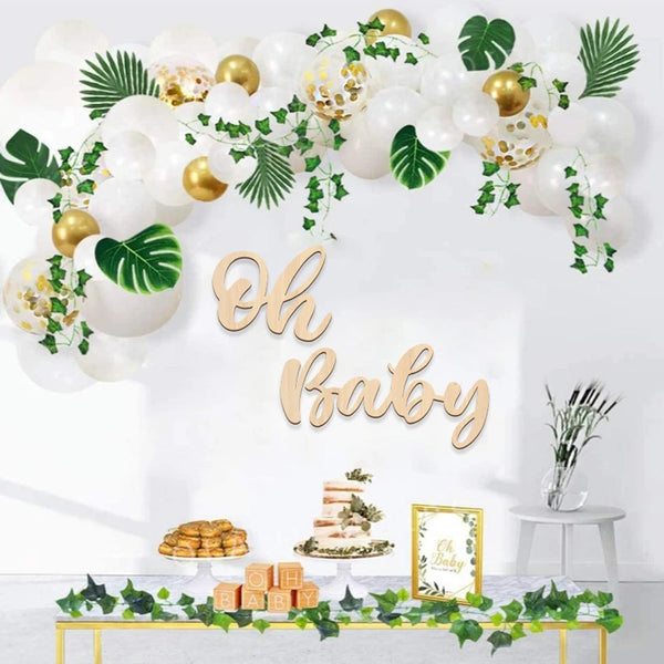 A wooden sign spelling out Oh Baby decorated with white balloons and green foliage for a baby shower