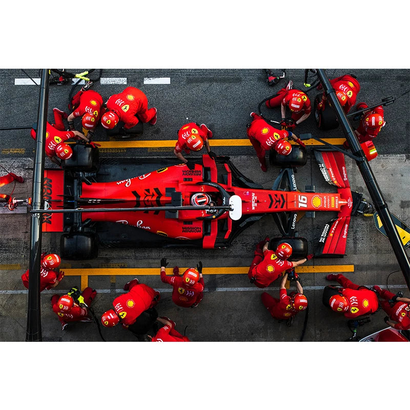 Un grupo de pilotos de Fórmula 1 con trajes rojos en la pared de boxes junto a un coche rojo y negro.