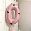 A pink foil balloon shaped like the number zero with black bows, hanging on a white door.
