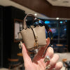 A hand holds a beige mini house handbag with a gold clasp and a colorful striped wrist strap.