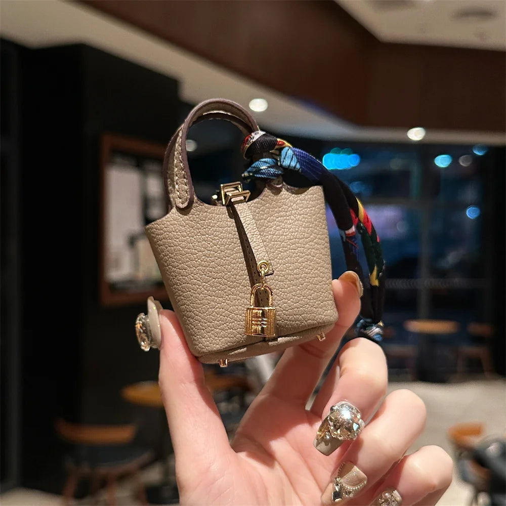A hand holds a beige mini house handbag with a gold clasp and a colorful striped wrist strap.