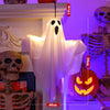 A white ghost decoration hangs on a shelf next to various skull and skeleton Halloween decorations.