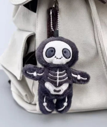 A dark gray mummy skeleton plush keychain is visible inside a light beige fabric bag.