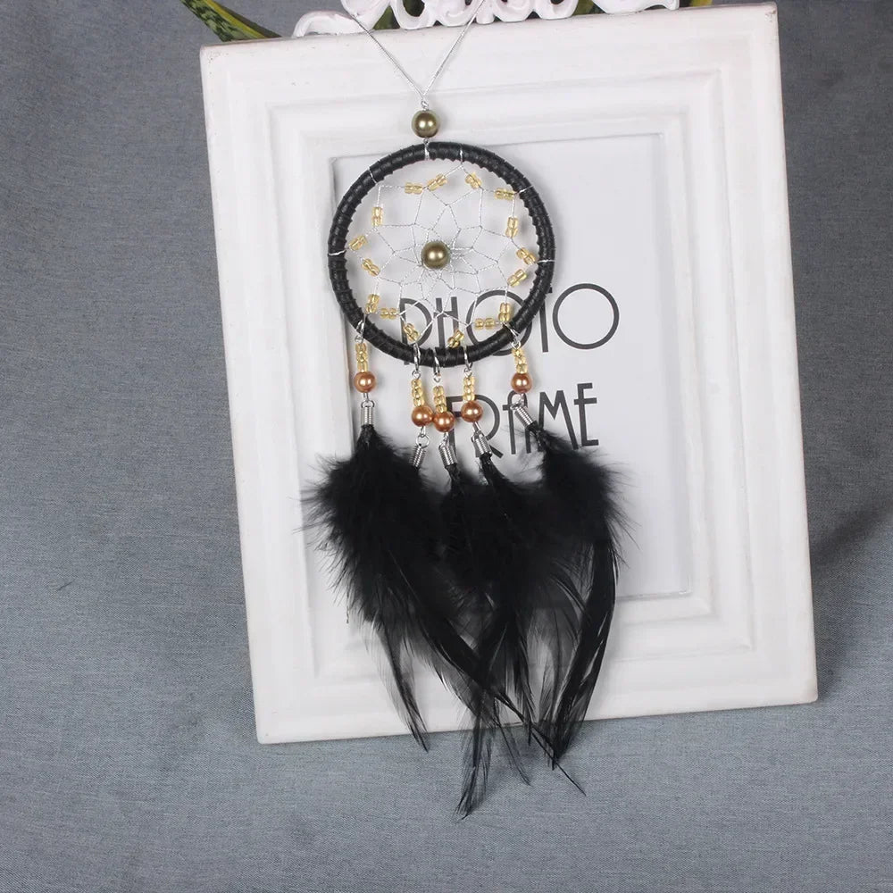 A black feather pendant charm with gold accents displayed in a white picture frame.