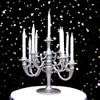 A silver candelabra holding nine white candles on a white cake with scattered gold and silver stars.