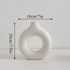 A white, modern ceramic circular vase with a smooth, organic shape, shown against a light background.
