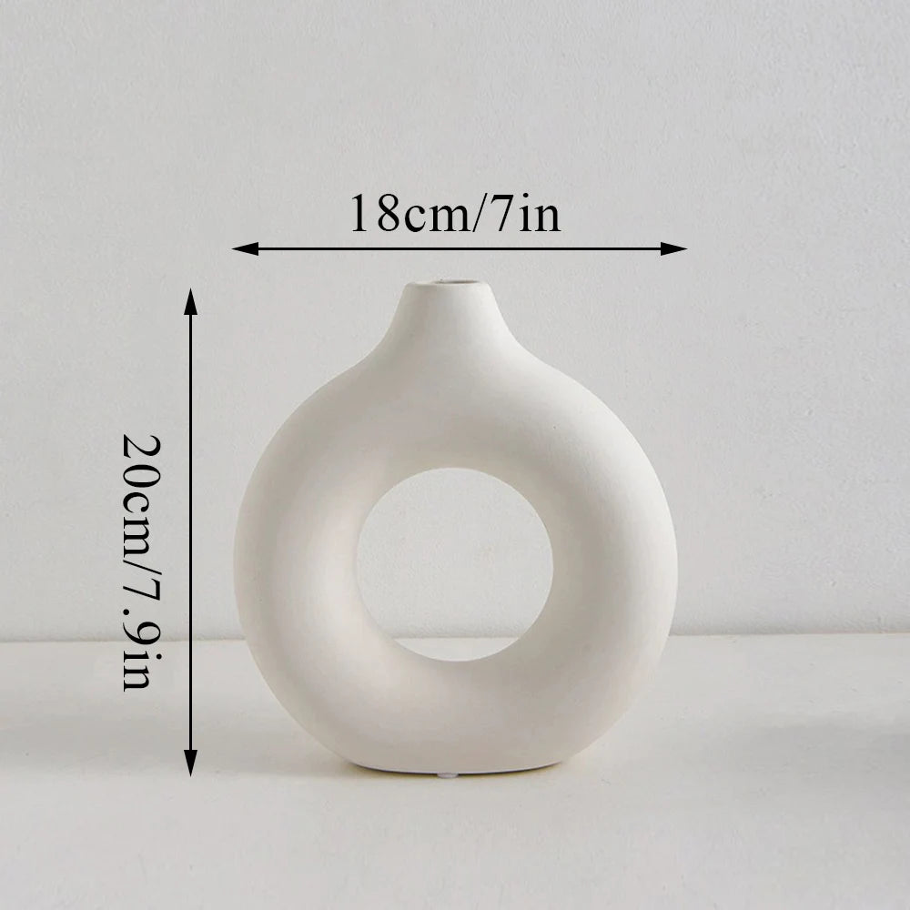 A white, modern ceramic circular vase with a smooth, organic shape, shown against a light background.