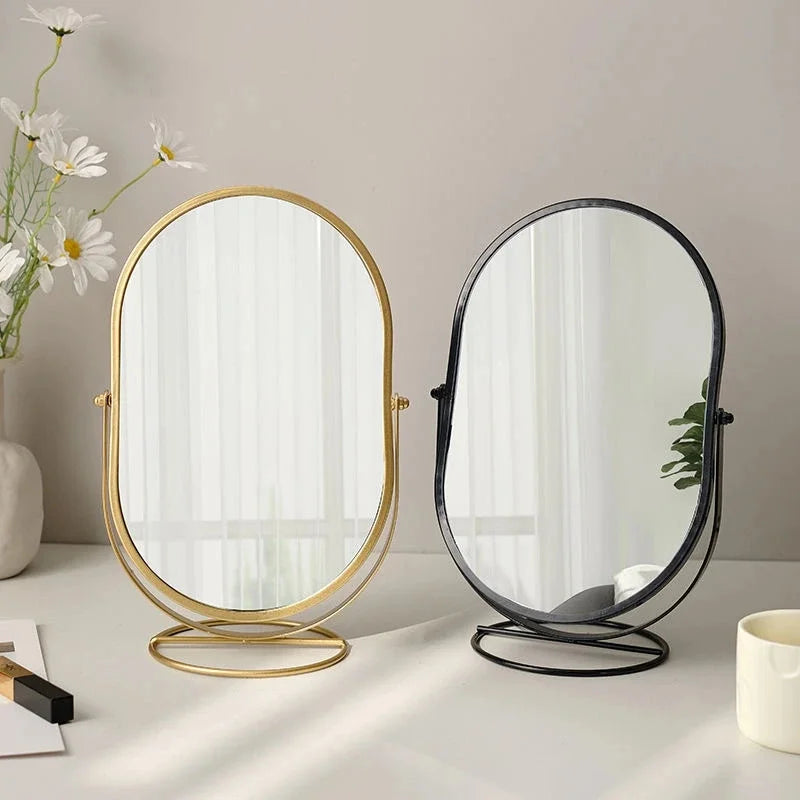 Elegant rotating oval vanity mirror with gold and black framing on a light surface.