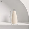 A tall, smooth, beige ceramic vase with a conical shape displayed on a white shelf.