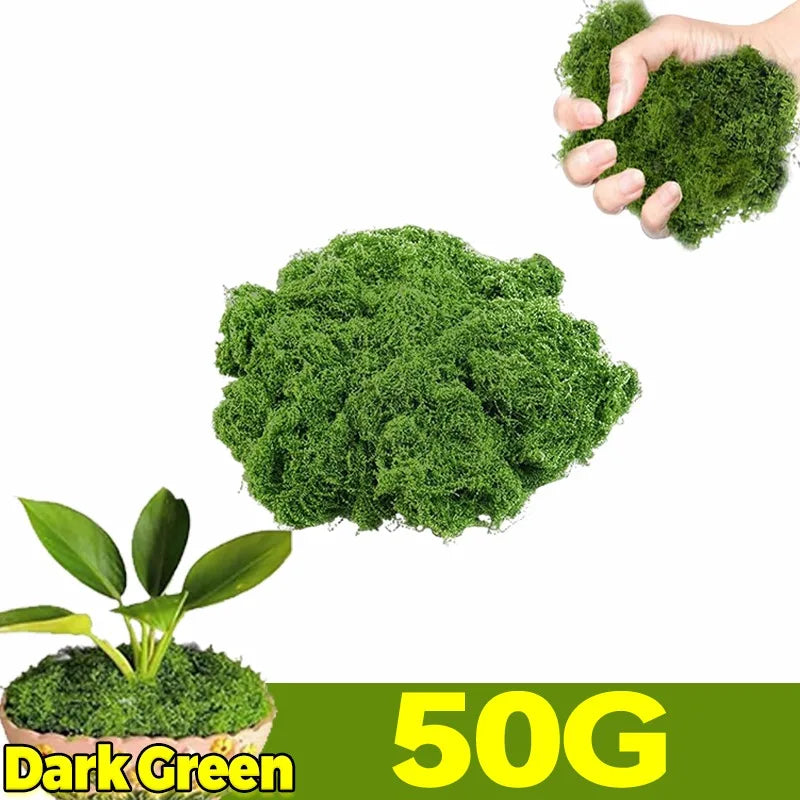 A hand is holding a clump of dark green artificial moss next to a pile of the same product.
