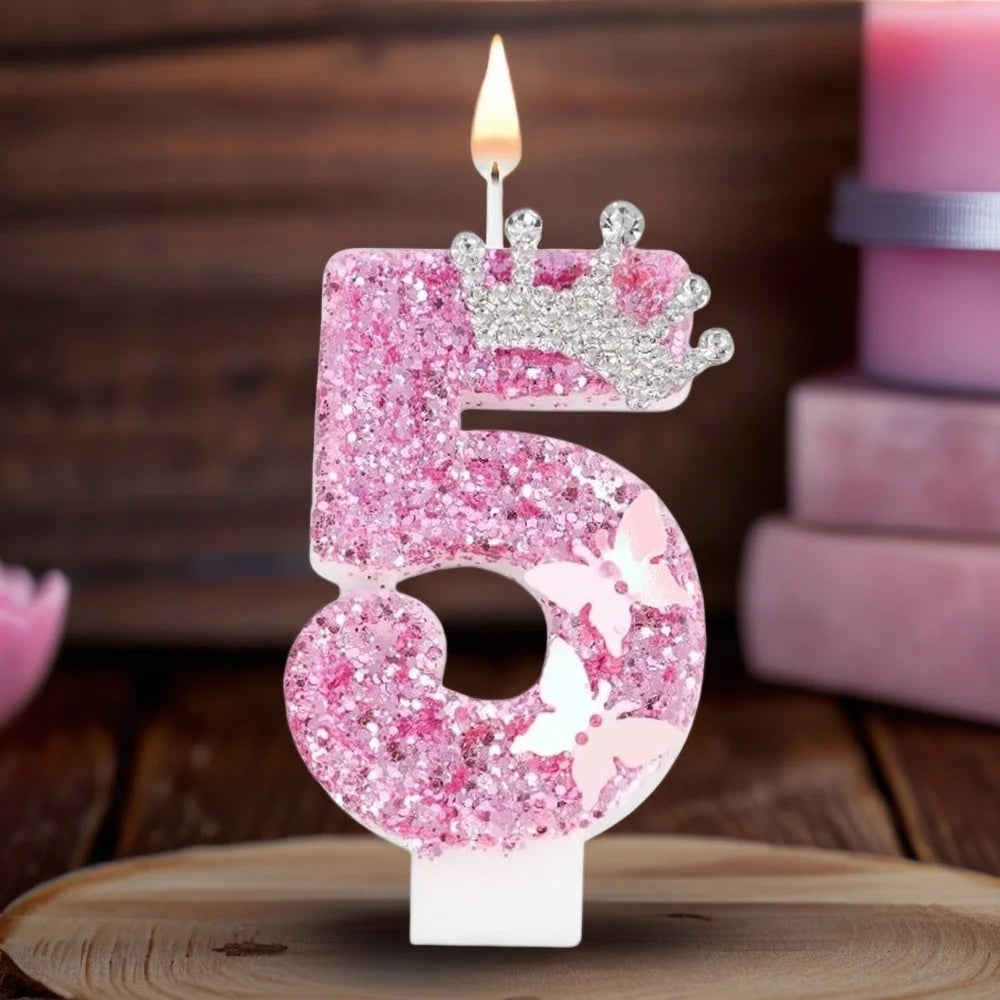 A pink glitter candle shaped like the number 5 with a crown on top, set against a wooden background.