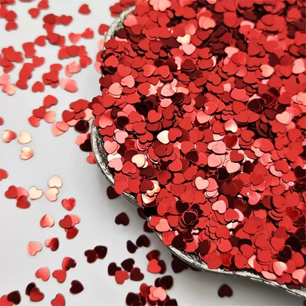 A close-up of red heart-shaped foil confetti scattered on a white surface.